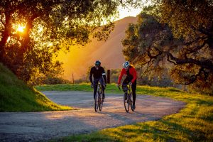 Two cyclists riding on Santa Rosa Creek Road in Cambria, California at sunset.