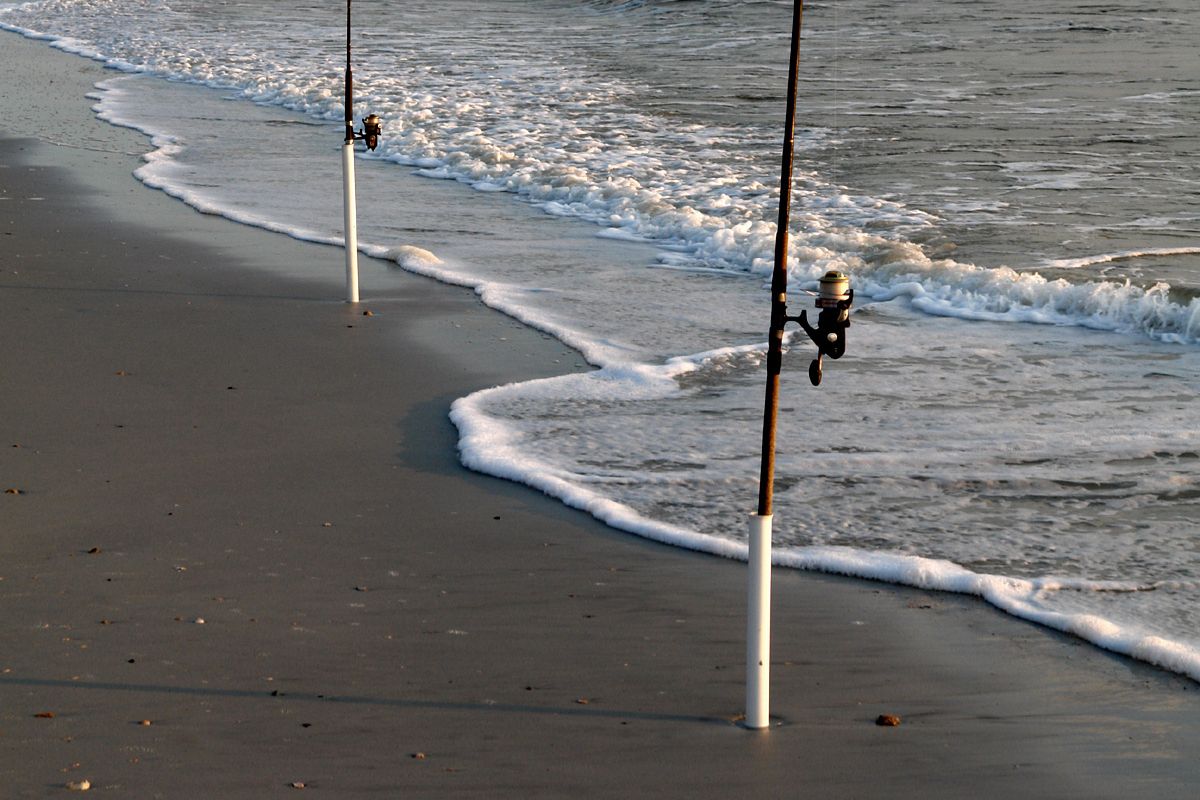 Two fishing poles affixed to the beach shore for surf fishing