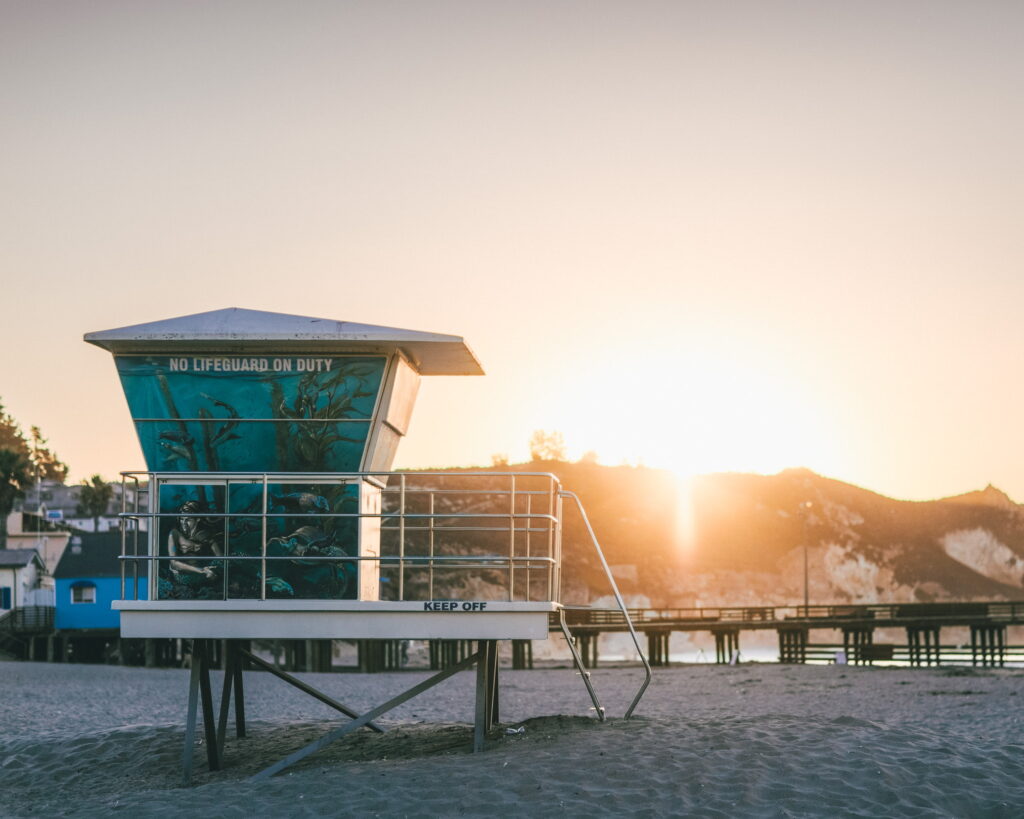 A teal lifeguard tower with a sloped ramp during a sunset.